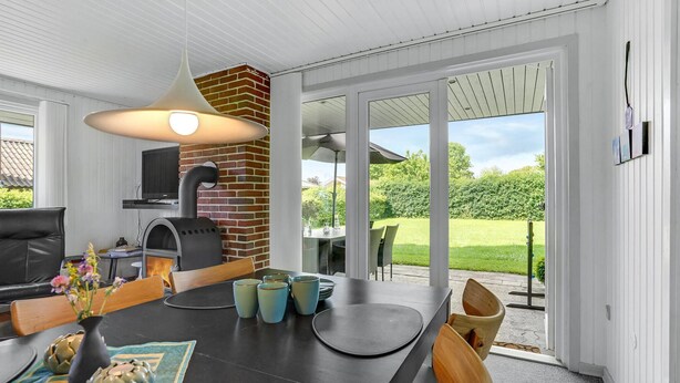 Une cuisine moderne dotée d’un four en briques, un coin repas avec une table dressée pour deux personnes et une grande porte-fenêtre coulissante donnant sur un jardin.