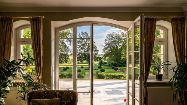 A room with a large sliding glass door leading to a garden. There are potted plants inside and on the windowsill.