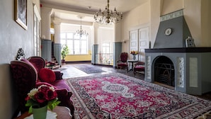 A spacious living room with a large red and blue patterned rug, a fireplace, and a chandelier.