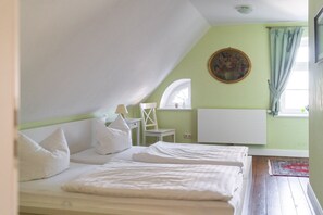 Una habitación pequeña y limpia con dos camas, una silla, una mesa y un ventanal con cortinas.