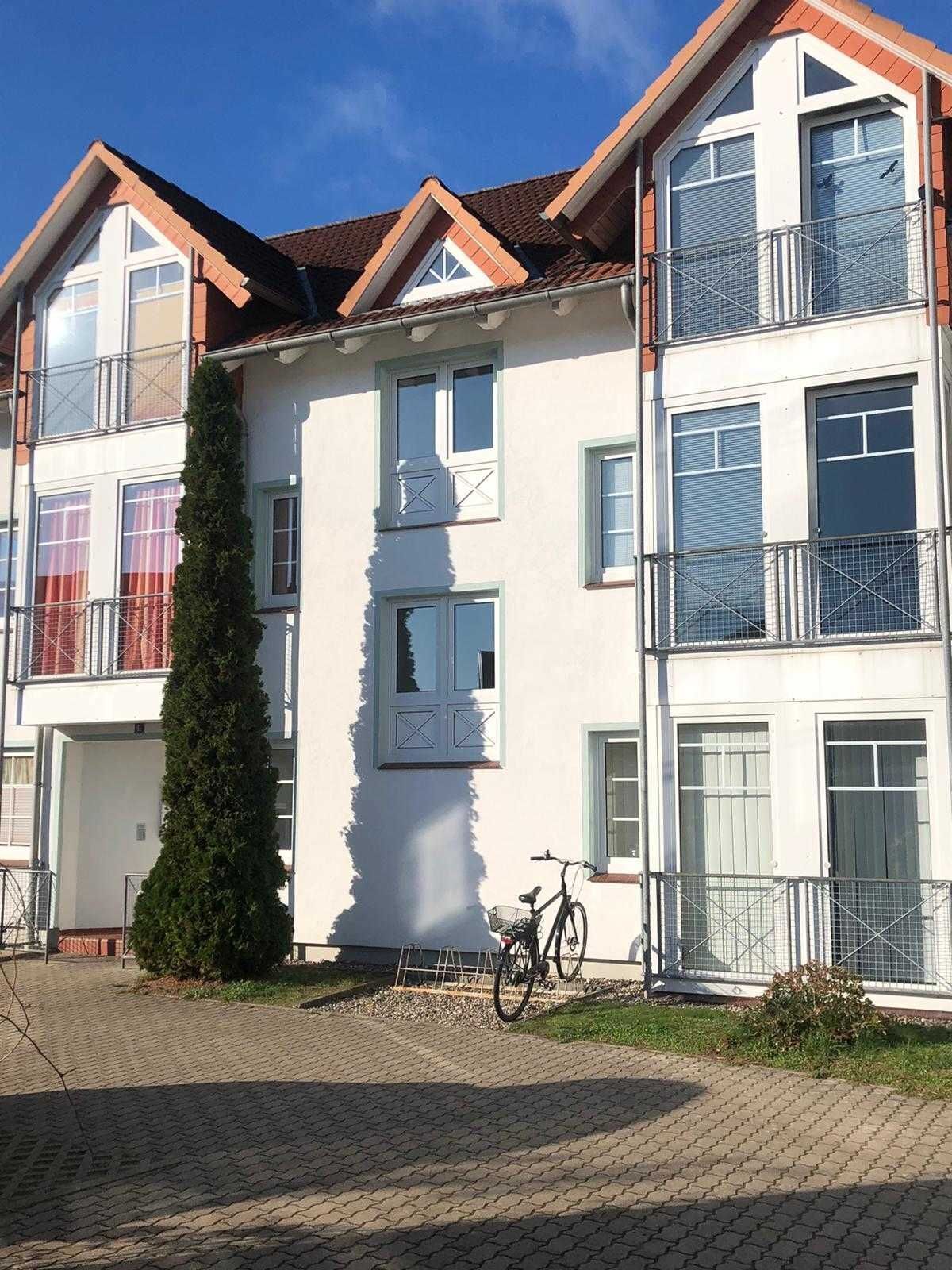 Un edificio residencial de varios pisos con entrada central, una bicicleta estacionada afuera y un jardín bien cuidado.
