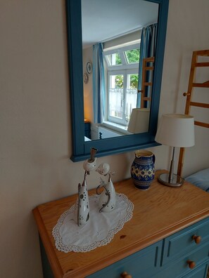 A room with a wooden dresser, a mirror, a vase, and a lamp.