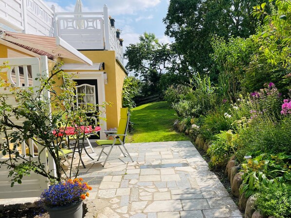 A pathway leading to a building with a yellow facade, a white gate, and a garden with various plants and flowers.