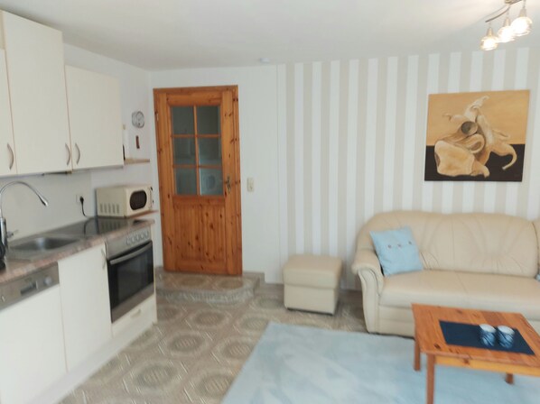 A compact living space with a kitchenette, a sofa, a coffee table, and a painting on the wall.