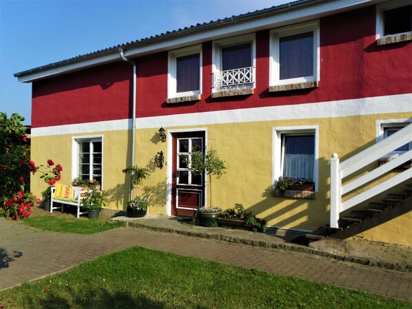 A two-story building with a red and yellow facade, a white staircase, and a small porch with potted plants.