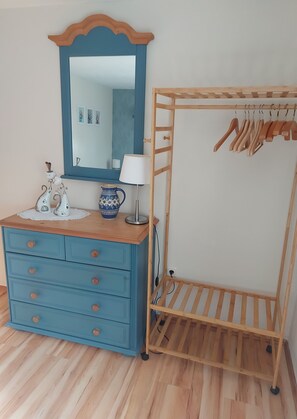 Ein Zimmer mit Kommode, Spiegel, Lampe und einem Kleiderständer aus Holz.