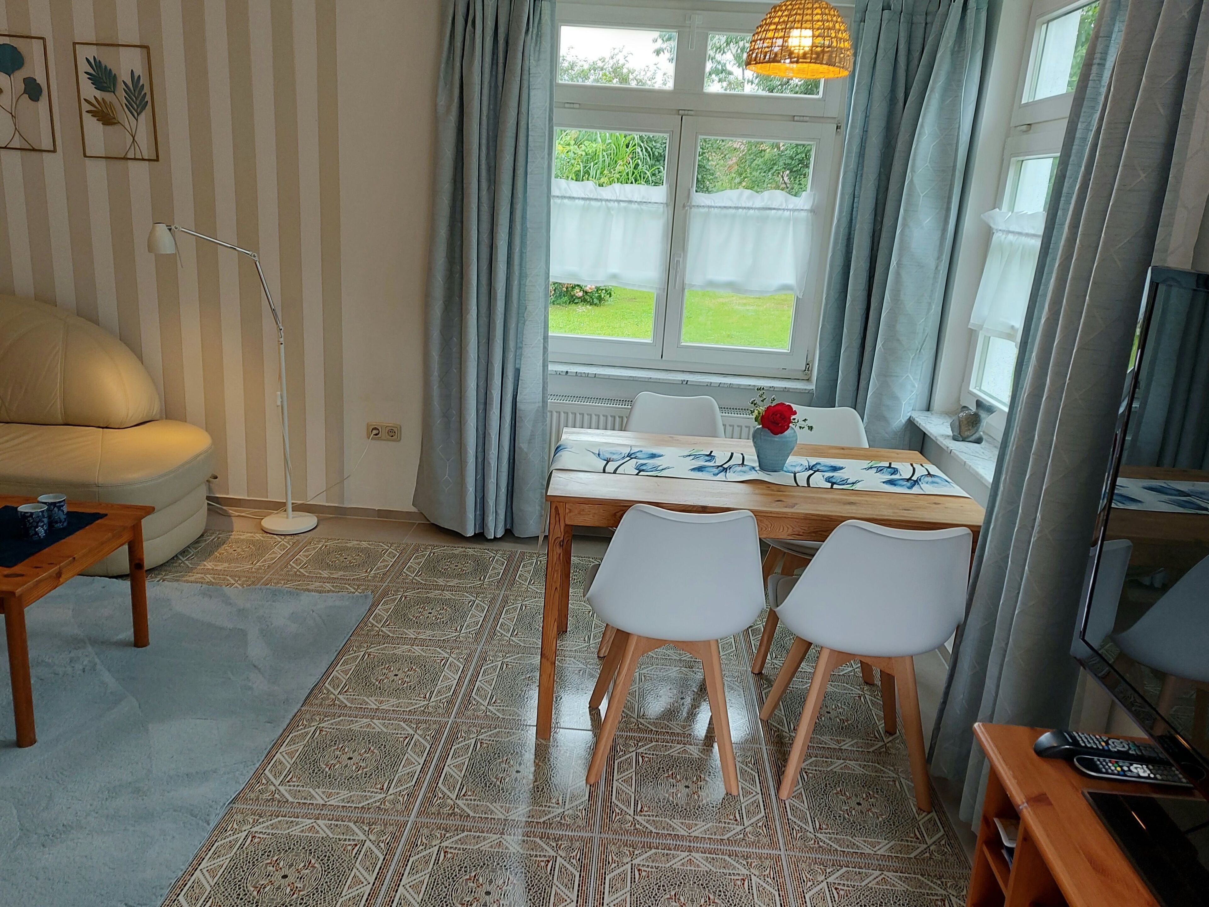 Ein Zimmer mit einer Couch, einem Esstisch mit Stühlen, einer Stehlampe und einem Fernseher.