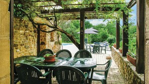 An outdoor patio with a stone wall, a table with chairs, and a view of a pool and garden. - Beautiful home in Monpazier (Monpazier)