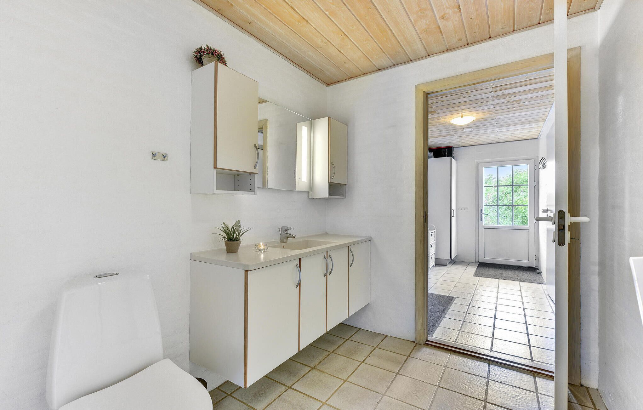Een badkamer met toilet, wastafel, spiegel en kastjes. Op de wastafel staat een potplant.