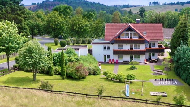 A two-story building with a red roof, surrounded by a well-maintained lawn and trees.