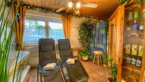A room with two reclining chairs, a ceiling fan, a window with curtains, and a cabinet with bottles.