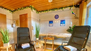 A room with two black chairs, a wooden table, a bathtub, a clock, and a plant.