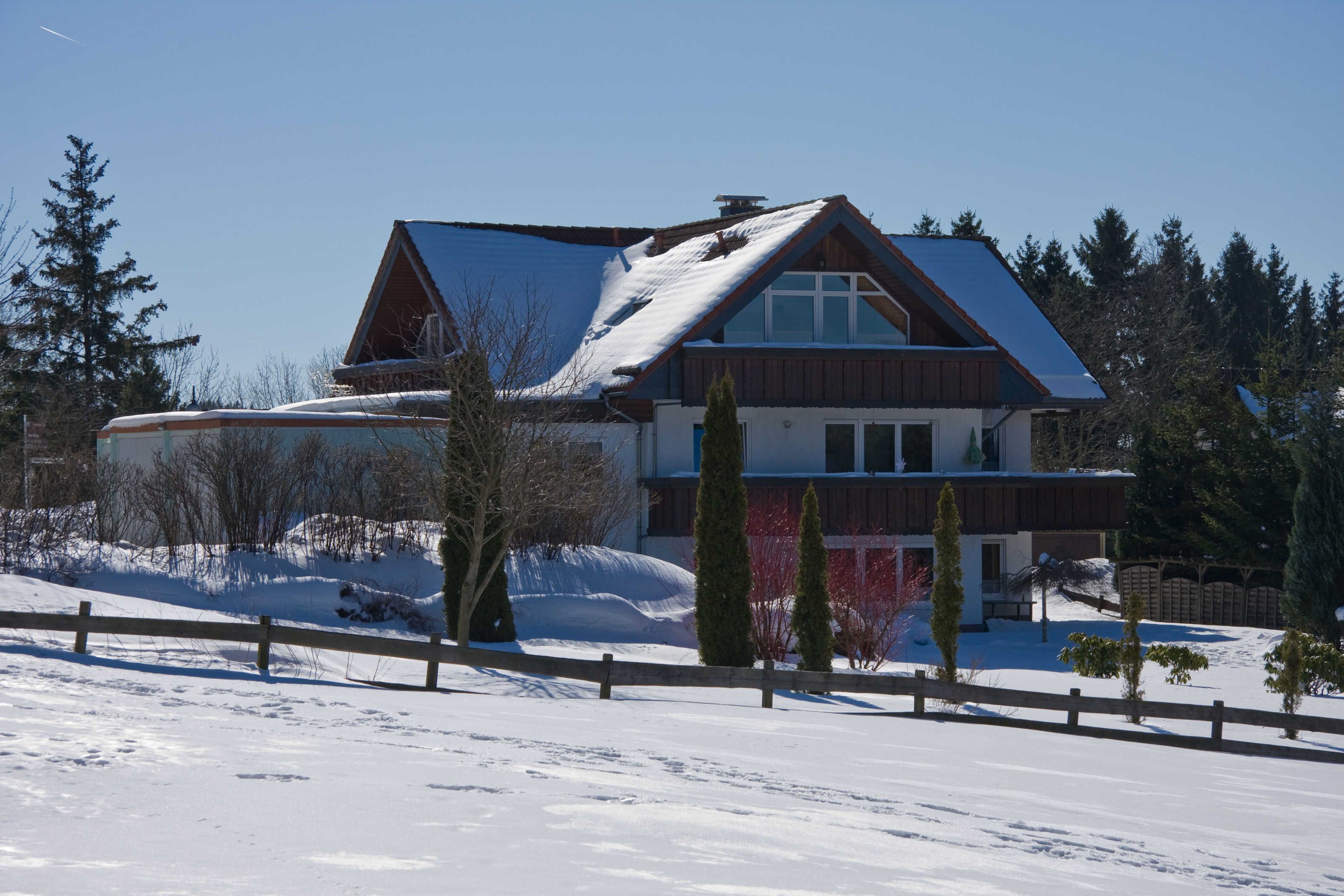 A two-story house with a sloped roof, surrounded by snow-covered ground and trees.