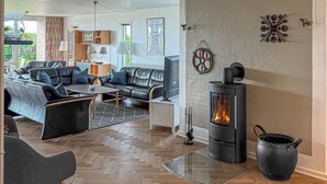 A modern living room with a fireplace, leather sofas, a glass coffee table, and a herringbone wood floor. - Cozy home in Ringkøbing with sauna (Ringkøbing)