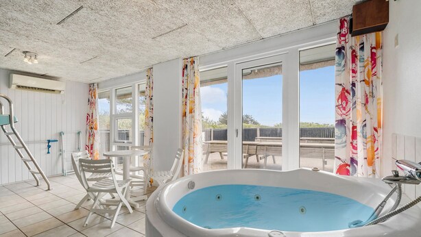 A sunlit room with a large window, a hot tub, and a table with chairs. - Cozy home in Ringkøbing with sauna (Ringkøbing)