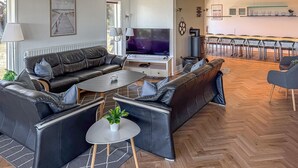 A modern living room with a sofa set, a TV, a dining area with chairs, and a kitchen in the background. - Cozy home in Ringkøbing with sauna (Ringkøbing)