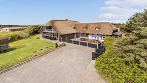 A large thatched-roof building with outdoor seating and a spacious driveway. - Cozy home in Ringkøbing with sauna (Ringkøbing)