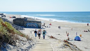 A beach with a wooden walkway leading to the shore, a large graffiti-covered structure, and people enjoying the beach. - Cozy home in Ringkøbing with sauna (Ringkøbing)