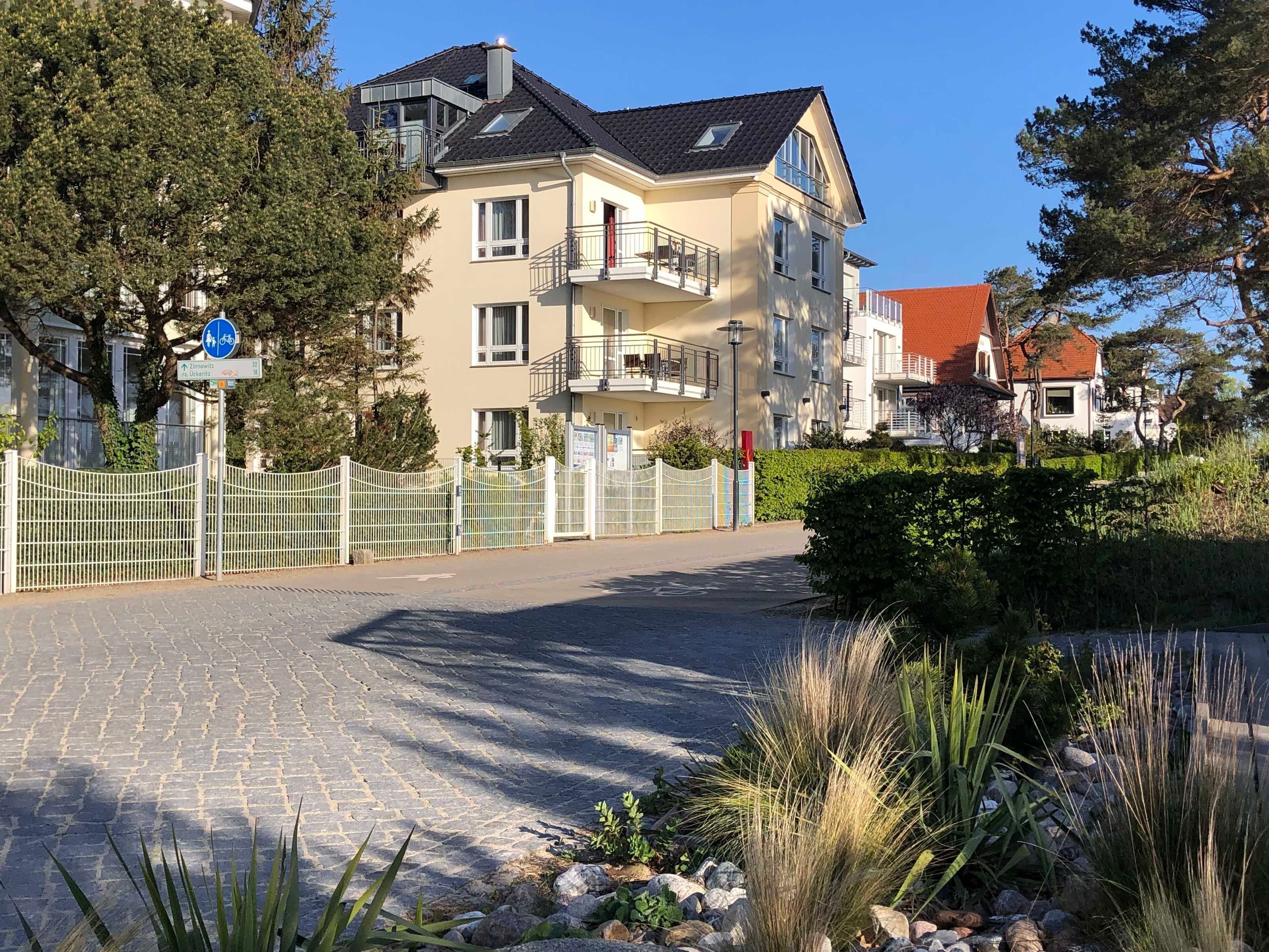 A multi-story residential building with balconies, a paved driveway, and a gated entrance.