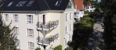A multi-story residential building with a sloped roof, balconies, and a well-maintained lawn.
