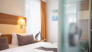 Habitación de hotel con cama, almohadas, lámpara, un cuadro y vistas al exterior.