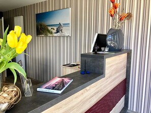 Una mesa de recepción con un cuadro enmarco de una escena de playa, un jarrón con flores secas y un libro titulado "EN JAHRE MIT EISEN".