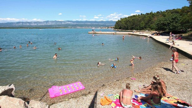 Una playa con agua cristalina, gente nadando y tomando el sol, y un litoral rocoso.