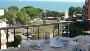 A balcony with a table set for two, overlooking a coastal view with buildings and a clear sky. - Holiday apartment near the beach (Porto Santa Margherita)
