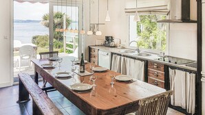 Un comedor con una mesa de madera dispuesta para cuatro, una cocina con lavaplatos y estufa, y vistas al exterior.