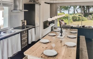 Una cocina moderna con una mesa de comedor de madera dispuesta para seis personas, horno empotrado y un amplio ventanal con vistas a un jardín.