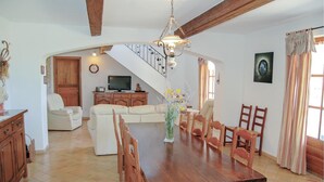 Ein geräumiger Wohnbereich mit Esstisch aus Holz, Stühlen, einer Couch und einem Fernseher.