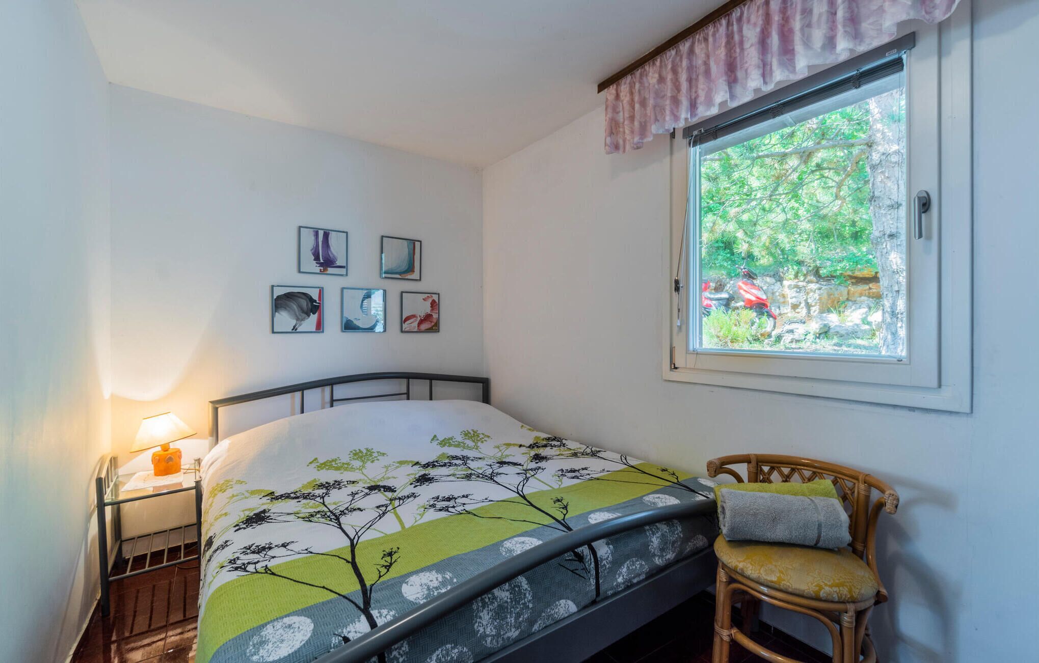 A bedroom with a bed, a chair, a window, and wall art.