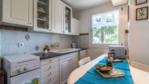 A compact kitchen with white cabinets, a built-in oven, and a window with a view of palm trees. - 2 bedroom beautiful home in Labin (Labin)