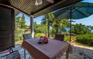 Eine Terrasse im Freien mit Tisch für zwei Personen, einer überdachten Sitzgruppe und Blick auf das Meer.