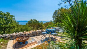 An outdoor seating area with a stone fire pit, two blue chairs, and a table with a yellow tablecloth. - 2 bedroom beautiful home in Labin (Labin)