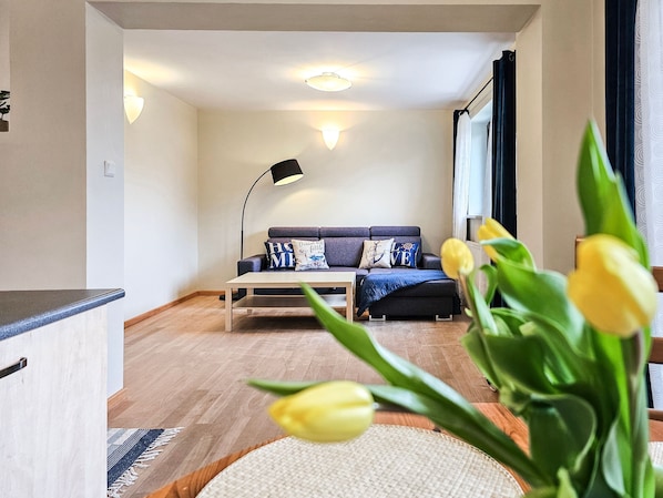 A modern living room with a sofa, a coffee table, and a floor lamp. There are yellow tulips in the foreground.