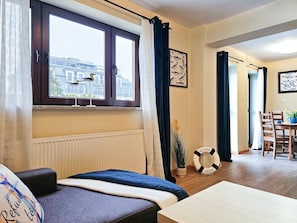 A cozy room with a bed, a small table, a window with curtains, a framed fish picture, and a life preserver on the floor.