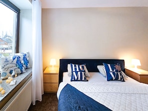 A hotel room with a bed, two bedside lamps, a window with a view of buildings, and decorative pillows.