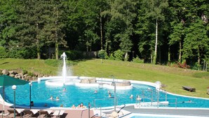 Une piscine avec une fontaine, entourée d’une pelouse et d’arbres.