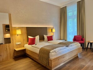 A hotel room with a wooden bed, two bedside lamps, a red chair, and a small table. - Single Room - Hotel Winterberg (Bad Harzburg)