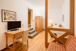 Een kamer met een houten bureau, een stoel, een bed, een televisie en een trap naar een houten garderobe.