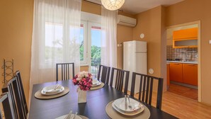 A dining area with a table set for four, a refrigerator, and an adjacent kitchen with orange cabinets. - Cozy home in Risika with WiFi (Risika)