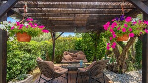 A wooden deck with wicker furniture, hanging flower pots, and a pergola structure. - Cozy home in Risika with WiFi (Risika)