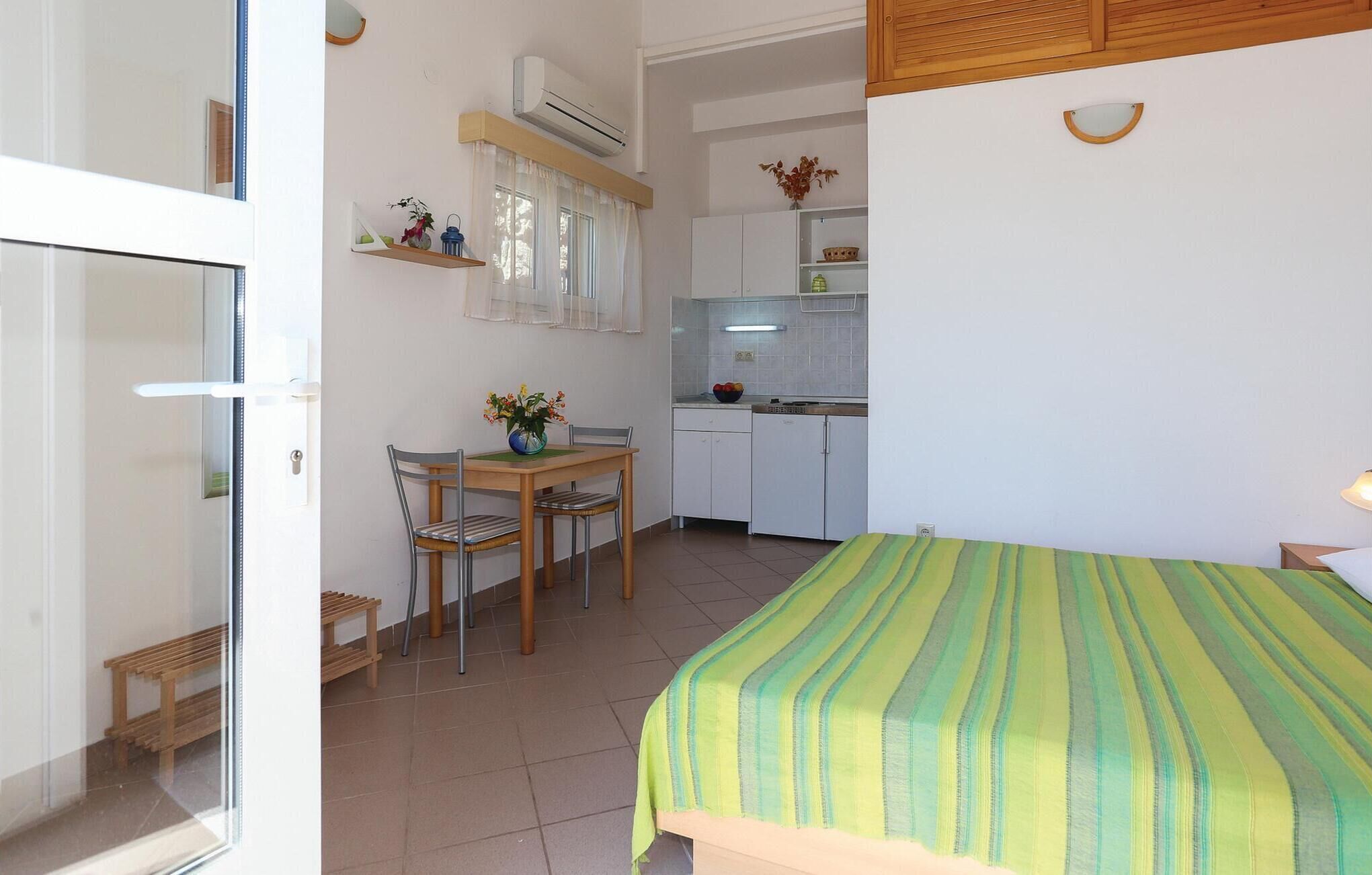 A small, clean room with a bed, a dining table with chairs, a kitchenette, and a bathroom.