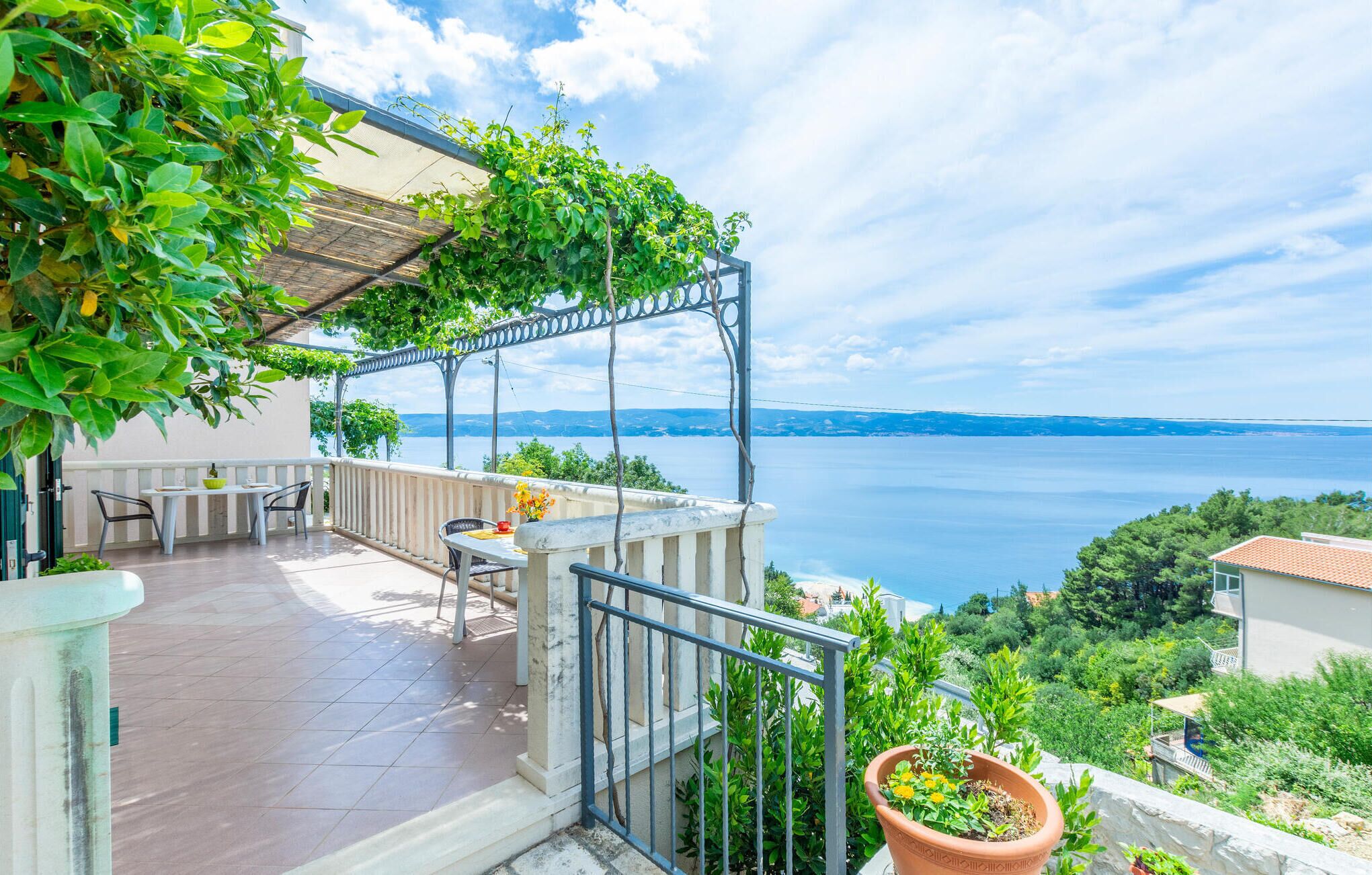 Ein Balkon mit Meerblick, einem Tisch mit Stühlen und einem Blumentopf.