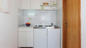 A compact kitchen with white cabinets, a sink, and a stove. There is a bowl of fruit on the counter and a green container on the shelf. - Nice apartment in Omis with WiFi (Omis)