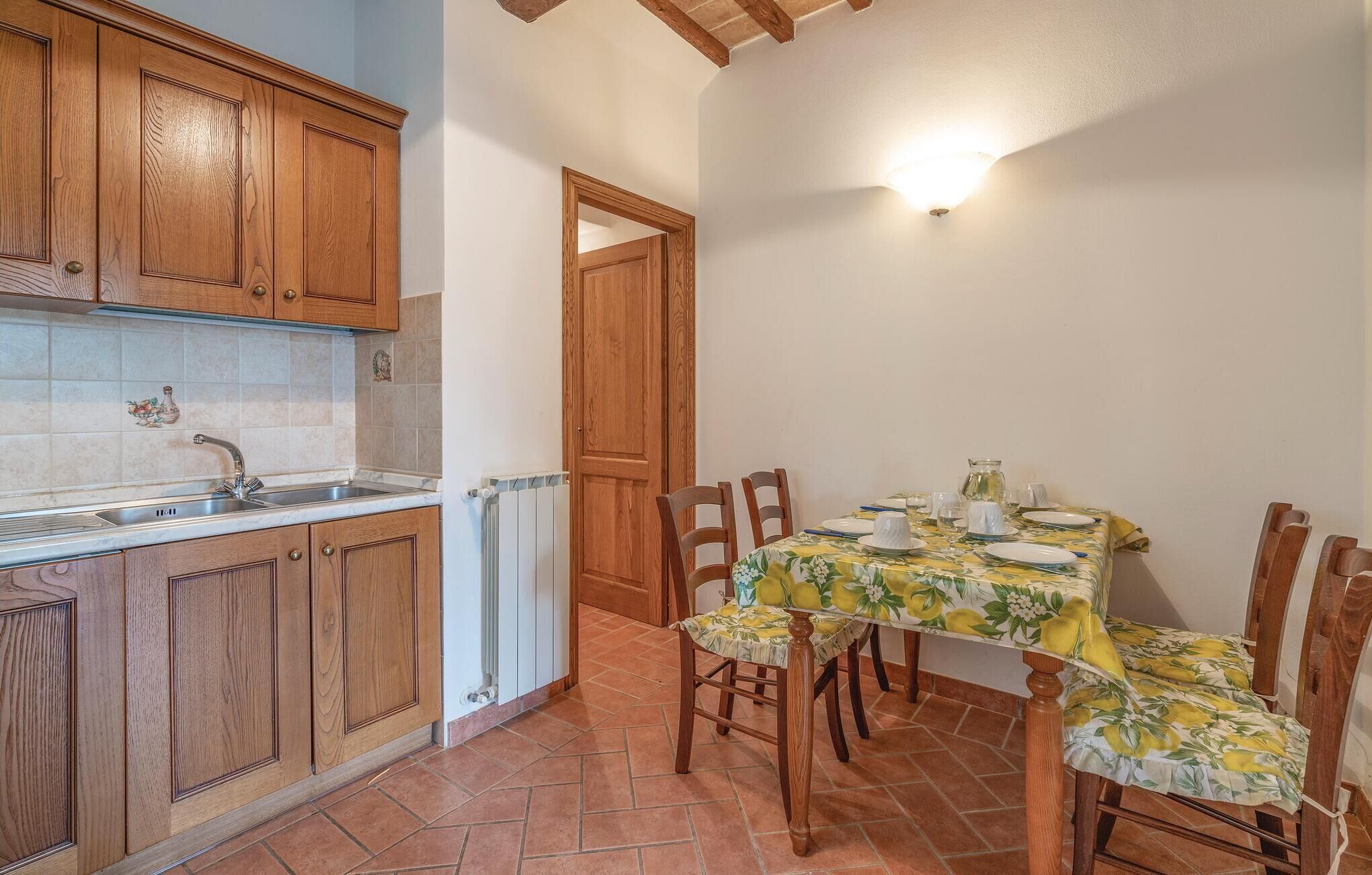 Une cuisine avec des meubles en bois, un dosseret carrelé et un coin repas avec une table dressée pour quatre personnes.