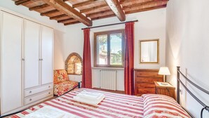 Ein Schlafzimmer mit Bett, Kleiderschrank, Schminktisch, Nachttisch, einem Fenster mit Vorhängen und einem Spiegel.