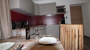 A dining area with a table set for two, a wine bottle, and a glass. The room has a red accent wall, a microwave, and a wooden chair. - Holiday apartment with infrared (Rauris)