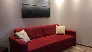 A red sofa with two pillows against a textured wall, with a painting above it. - Holiday apartment with infrared (Rauris)